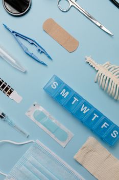 Flat lay of medical supplies including bandages, syringe, and face mask on a blue background.