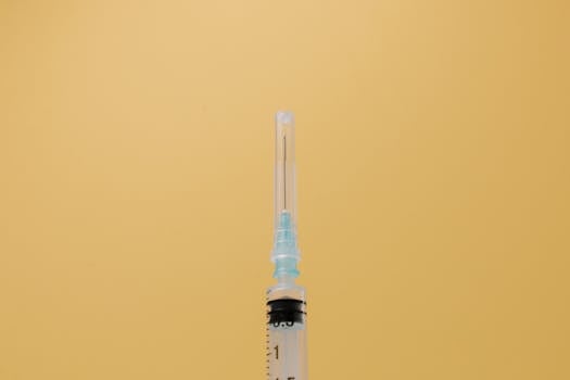 A close-up view of a syringe against a plain yellow backdrop, symbolizing healthcare.