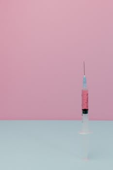 A medical syringe filled with pink liquid stands against a pastel background, perfect for health-related themes.