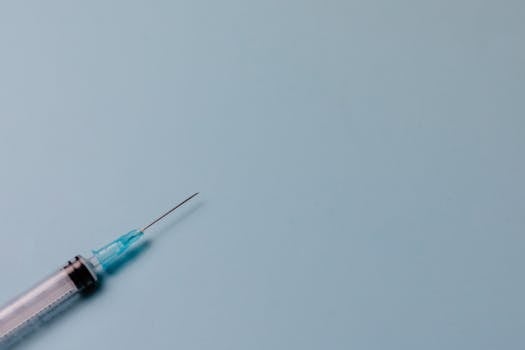 Detailed shot of a syringe against a pastel blue surface, ideal for medical themes.