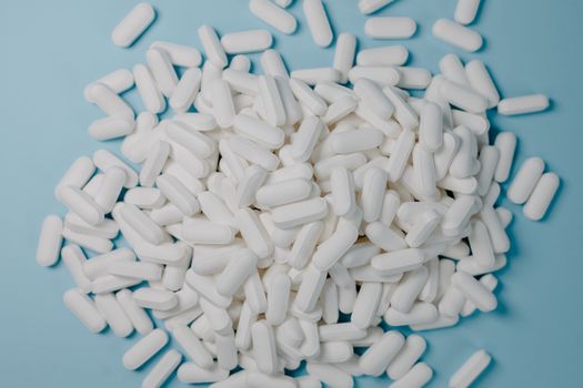 A collection of white oblong pills scattered on a blue surface, healthcare and medication concept.