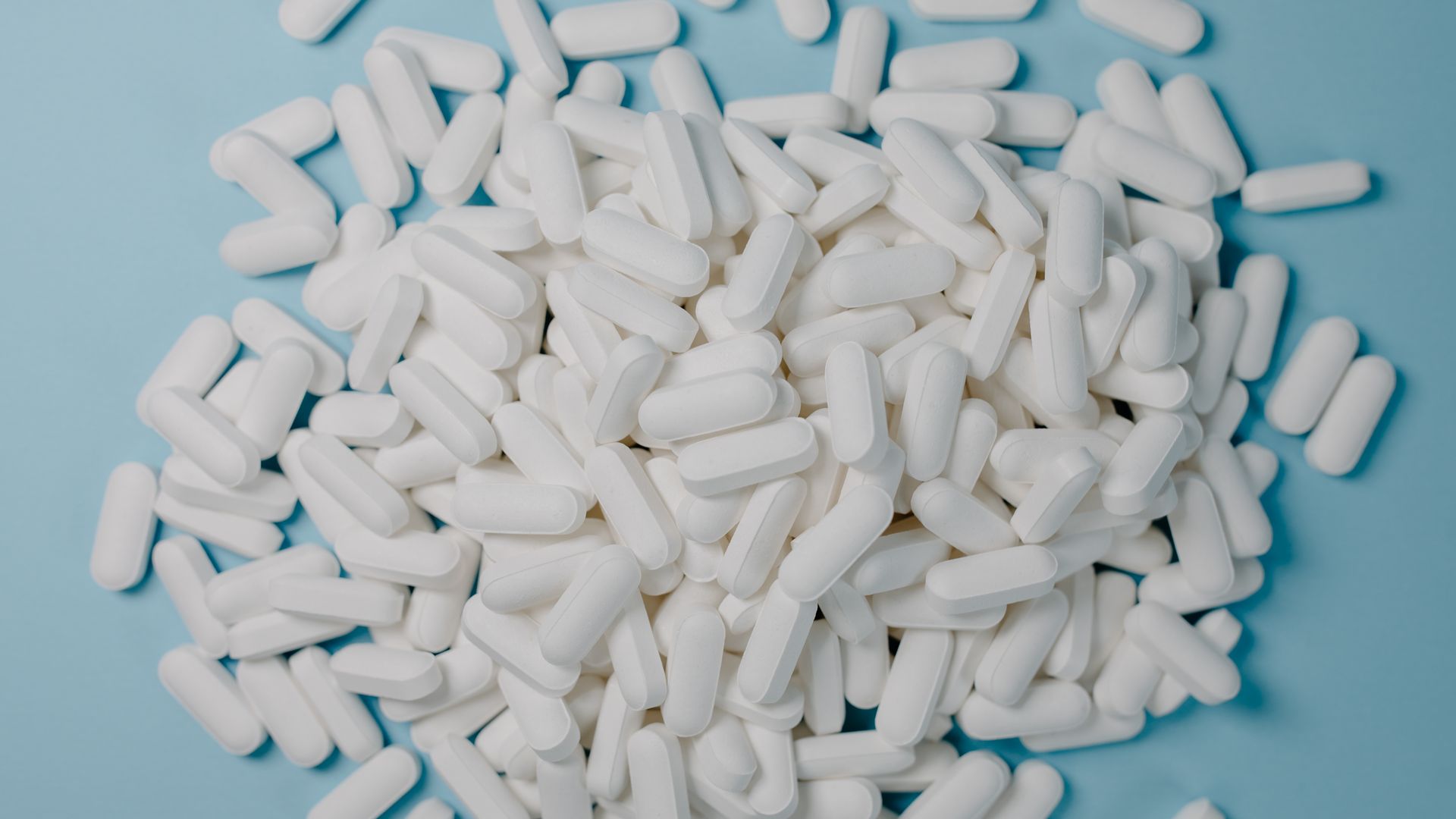Is Modafinil a Stimulant? Unlocking the Truth A collection of white oblong pills scattered on a blue surface, healthcare and medication concept.