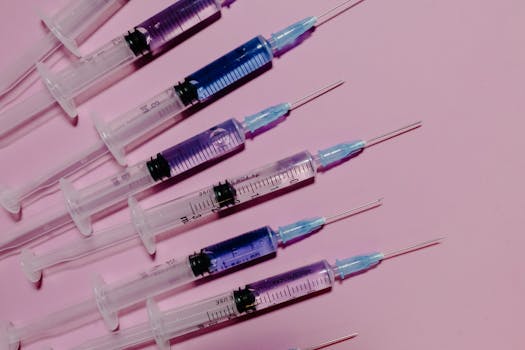 Several syringes with blue liquid on a pink background, showcasing medical equipment.