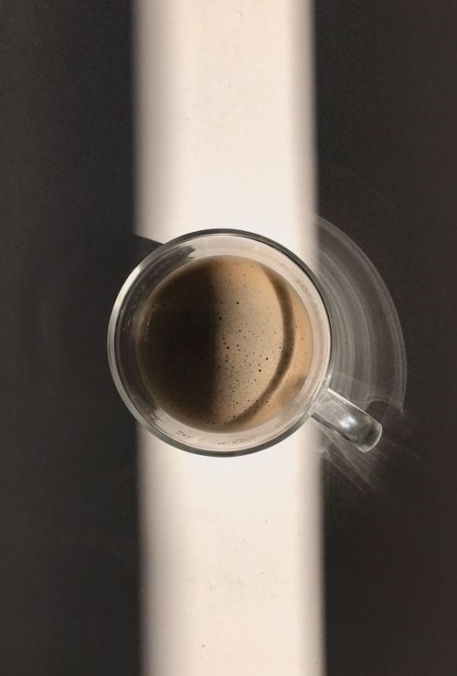 Free Aerial view of a glass mug with coffee casting shadows on a striped surface. Stock Photo