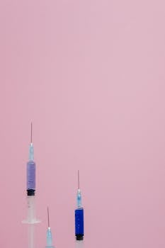 Three syringes of varying sizes stand against a pastel pink backdrop, ideal for medical themes.