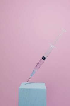 Simple composition of a syringe against a pink backdrop for medical themes.