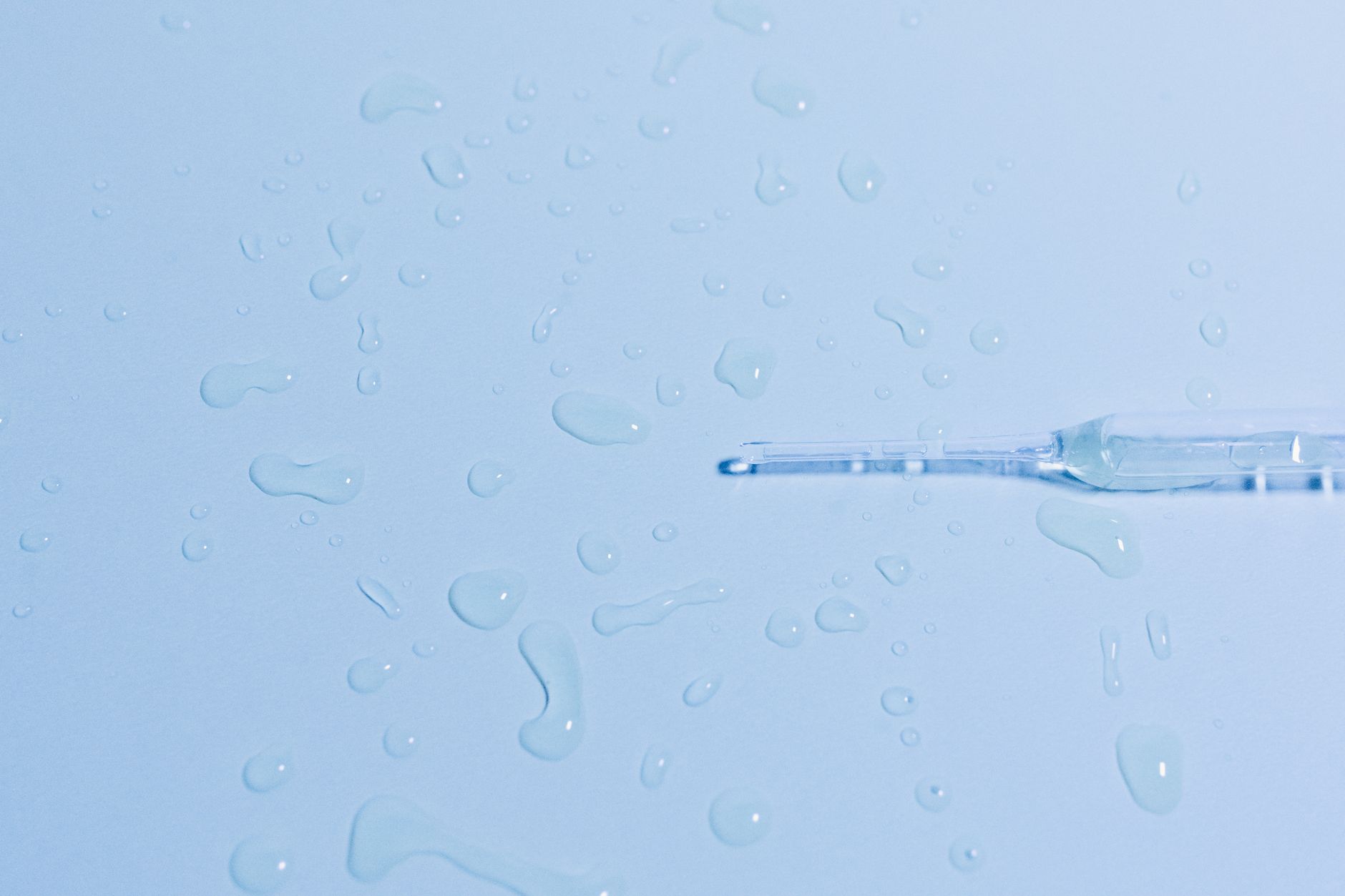 Detailed close-up of a glass pipette on a wet surface with scattered water droplets.