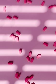 Scattered pink tablets on a light pink background with dramatic shadows creating a striped pattern.