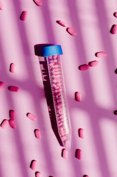 A centrifuge tube surrounded by pink pills on a pink background with shadow effects.