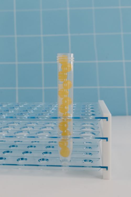 Free A yellow centrifuge tube stands on a blue test tube rack with a checkered background. Stock Photo