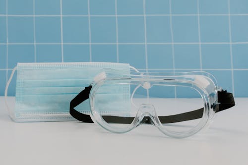 Close Up Photo of Disposable Facemask and Protective Goggles