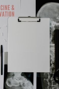 Top view of a blank clipboard, x-ray, and pills on a medical desk.