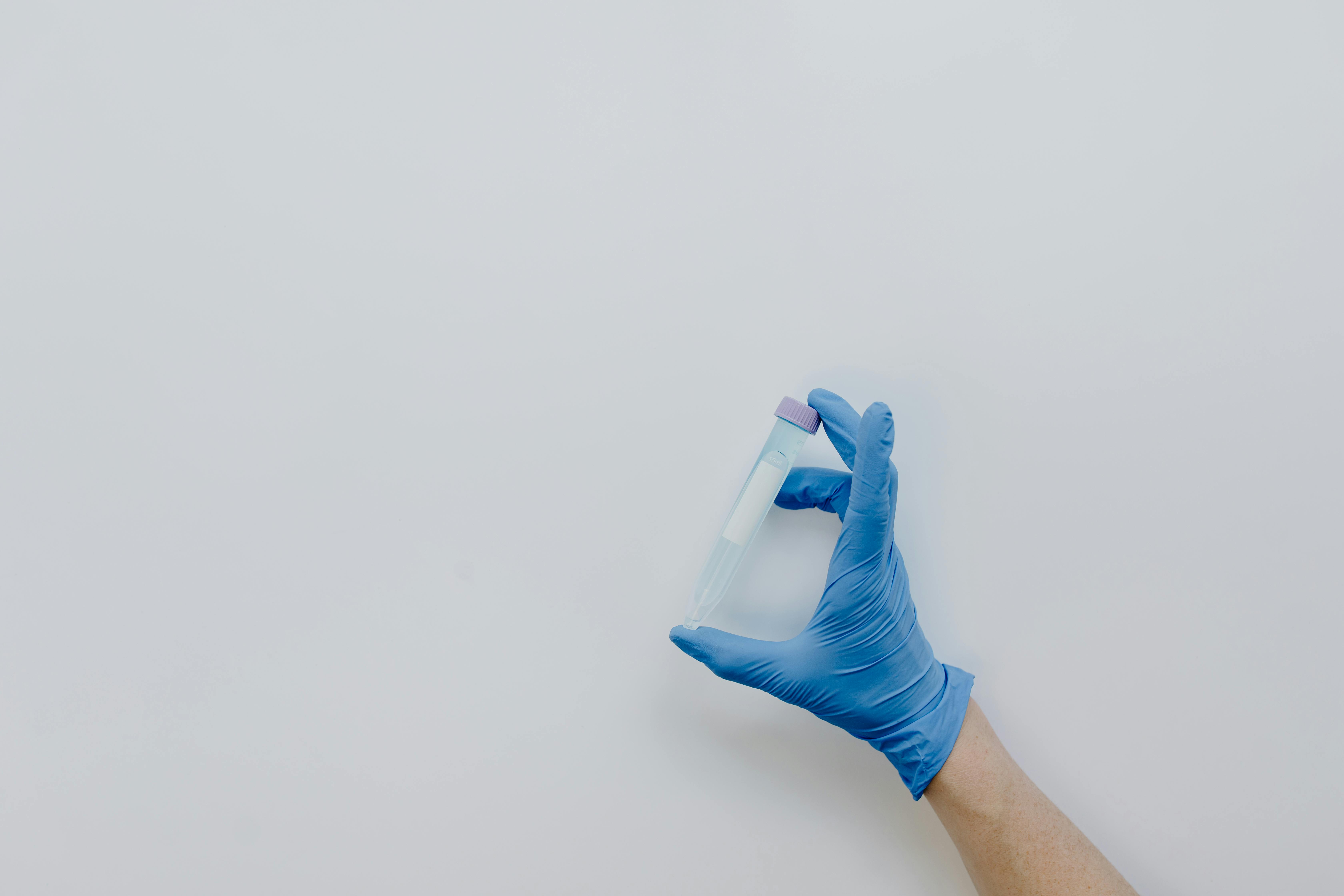 Gloved hand holding a centrifuge tube against a plain backdrop, offering copy space.