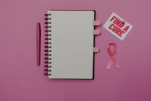 Free Flat lay of breast cancer awareness items, including pink ribbon and 'Find a Cure' message. Stock Photo