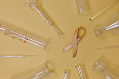 Top view of pink ribbon representing cancer placed on yellow background among glass test tubes and flasks in light studio