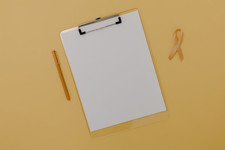 A White Blank Paper On A Clipboard Beside Brown Ribbon And Pen