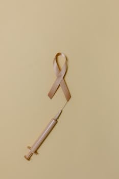 A beige awareness ribbon and syringe on a light background, symbolizing healthcare themes.