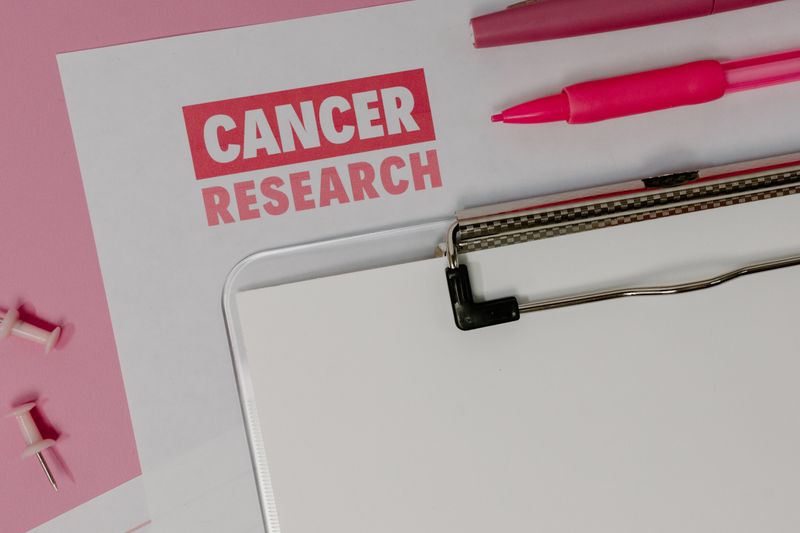 Flat lay of a cancer research paper on a clipboard with pink stationery items.