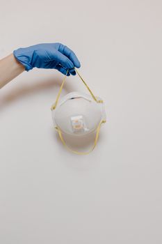 A gloved hand holding an N95 mask against a plain background, showcasing safety gear essentials.