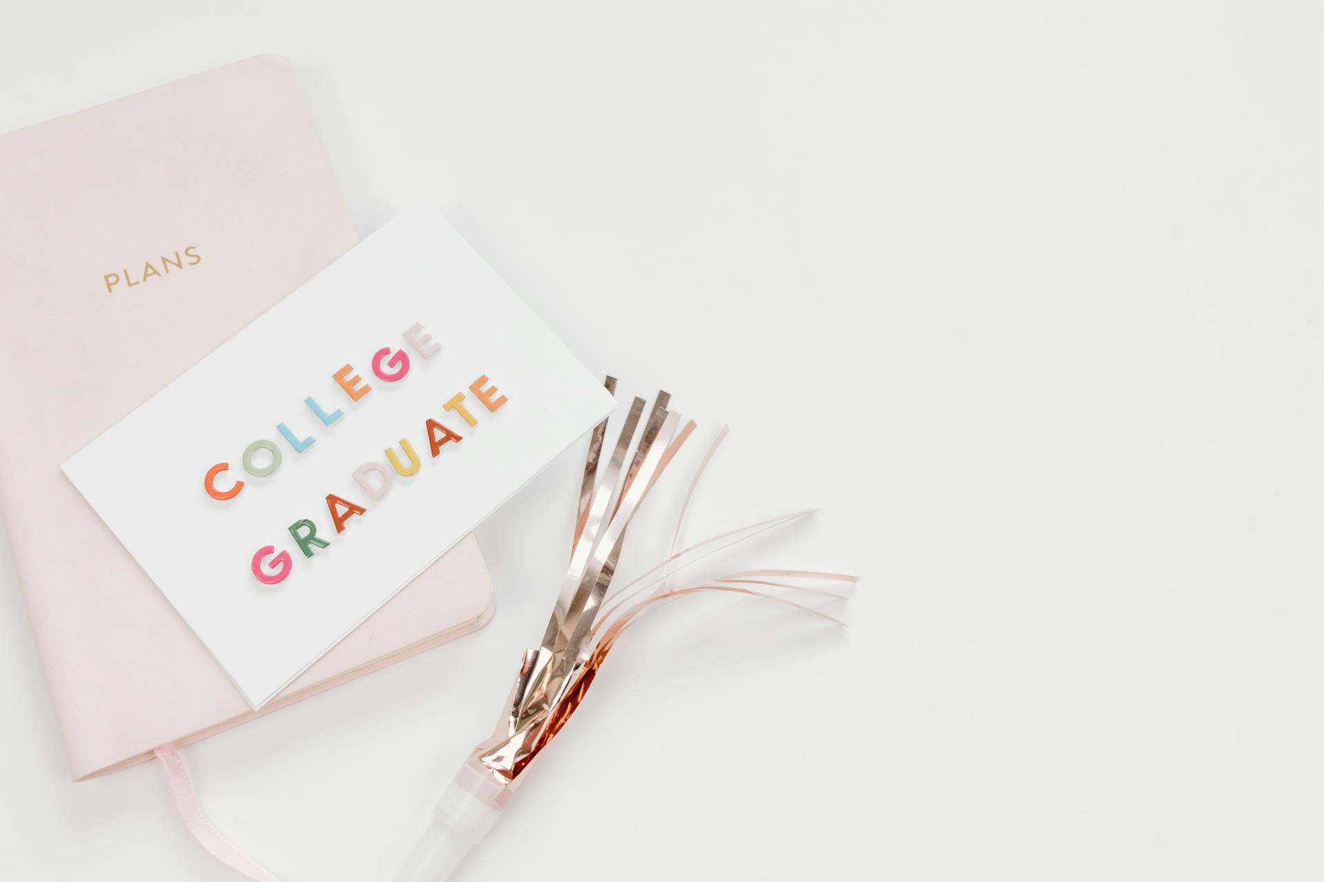 Elegant flat lay of a college graduate card with a notebook and party decor, perfect for celebration themes.