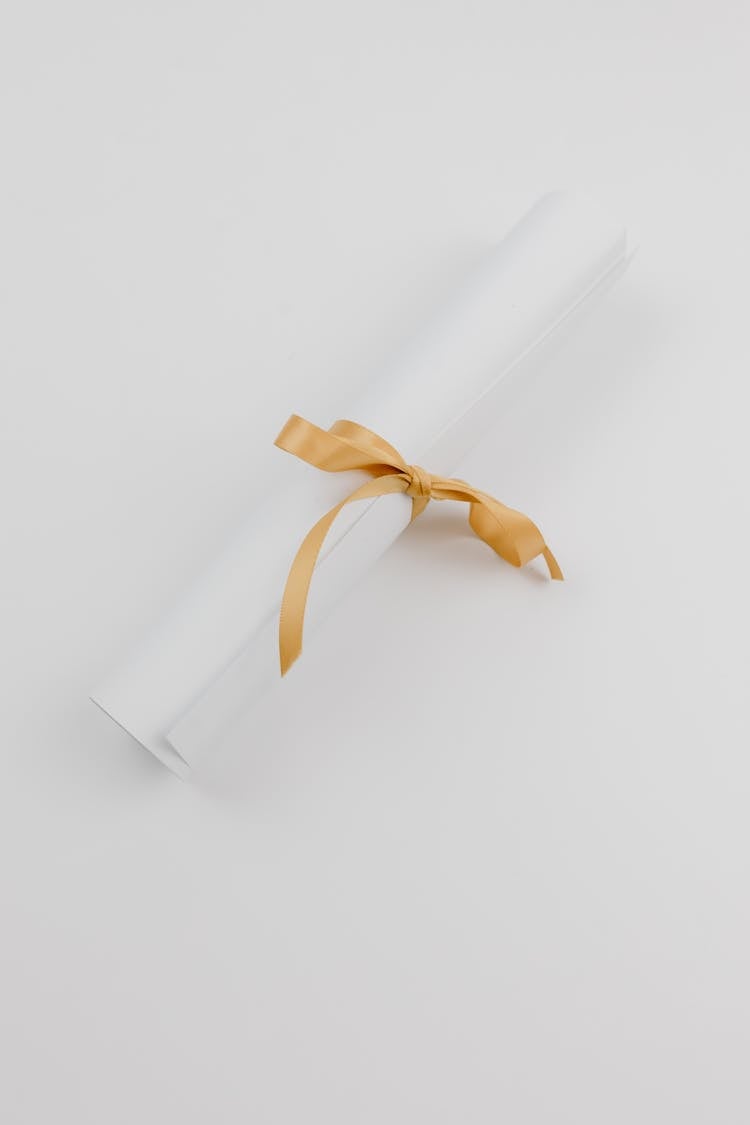 A Rolled White Paper With Gold Ribbon  