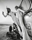 Black and white low angle of women in trendy outfit while riding outside of car on sandy beach