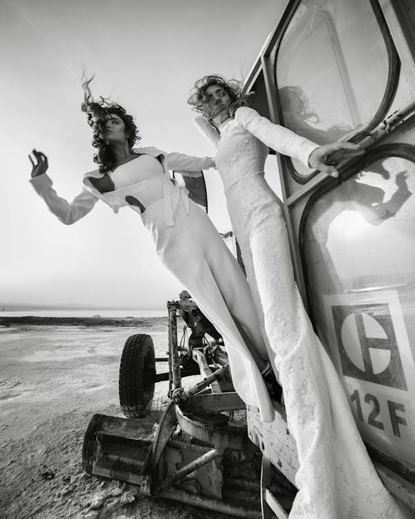Free Black and white low angle of women in trendy outfit while riding outside of car on sandy beach Stock Photo