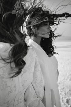 Black and white of ladies with long dark hair flying in wind on blurred background of beach