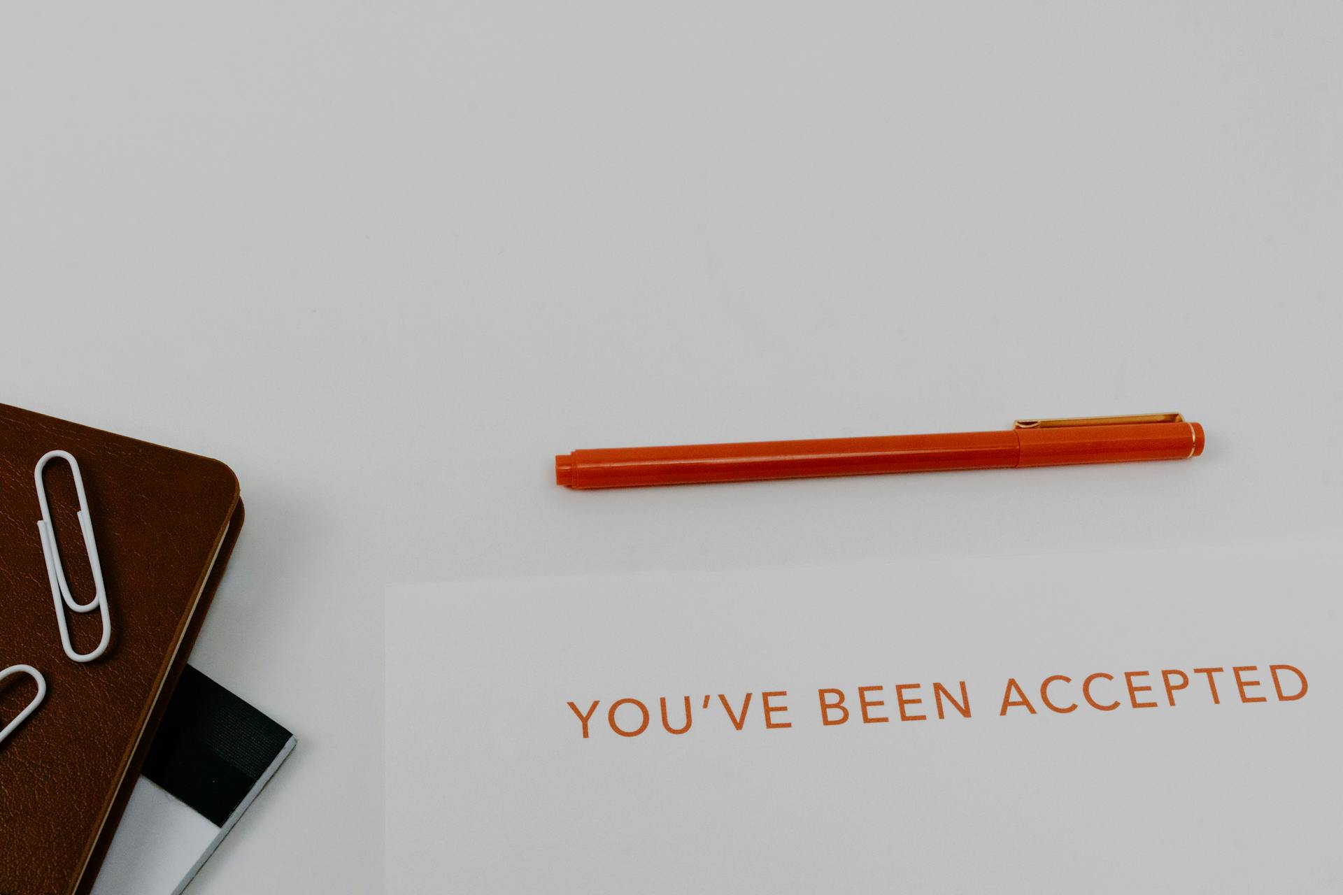 Close-up of an acceptance letter with a pen and planner on a white surface.