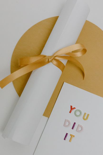 Rolled white certificate tied with gold ribbon on textured background next to congratulatory card. Rolled white certificate tied with gold ribbon on textured background next to congratulatory card.