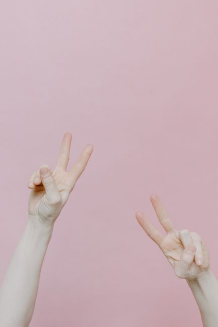 Fotomural Dos manos haciendo signos de paz sobre un suave fondo rosa.