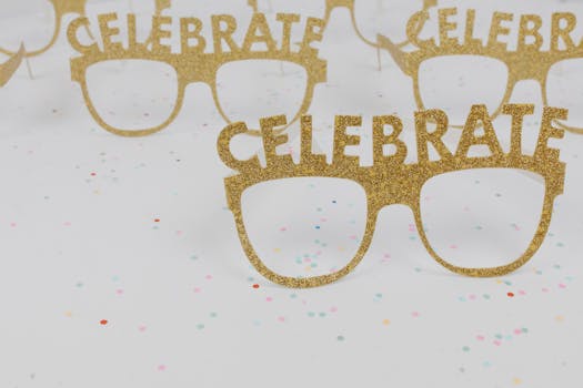 Sparkly gold 'Celebrate' eyeglasses on confetti background perfect for party decor and festive occasions.