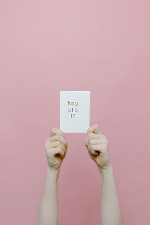 Free Hands holding a congratulatory card with 'You Did It' text against a pink background, conveying success. Stock Photo