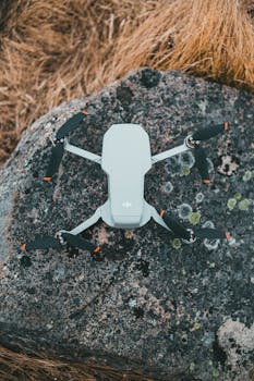 From above of modern white UAV placed on rocky surface near dried grass in countryside on autumn day in nature