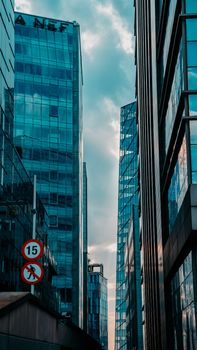 Vertical shot of skyscrapers with glass facades reflecting clouds in an urban setting.