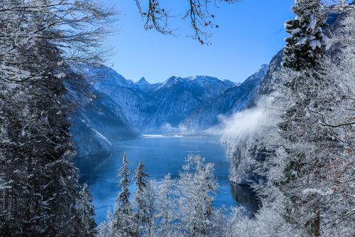 Free Serene winter landscape of a snowy lake surrounded by mountains and frosty trees. Stock Photo