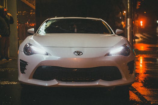 A white Toyota parked on a wet street at night, illuminated by city lights.