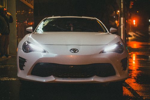 Free A white Toyota parked on a wet street at night, illuminated by city lights. Stock Photo