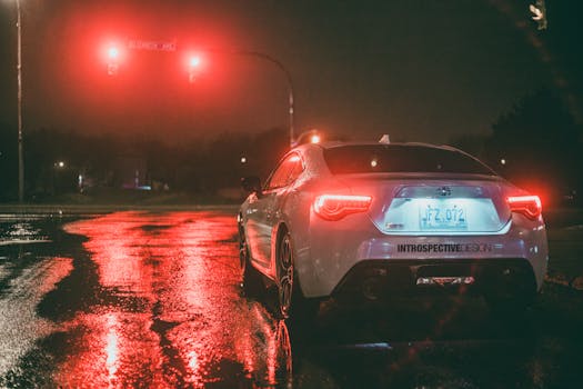 White car stopped at a wet urban intersection under red traffic lights at night.