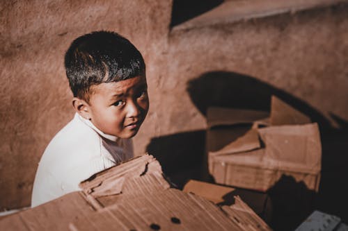 Free A Boy Sitting Beside a Cardboard Boxes Stock Photo