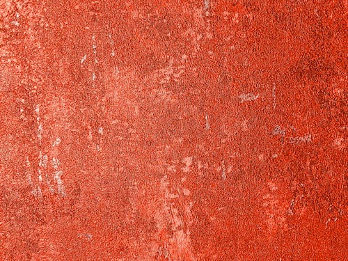 Background of textured shabby wall with red peeling paint and stains with spots of old fashioned building located on street