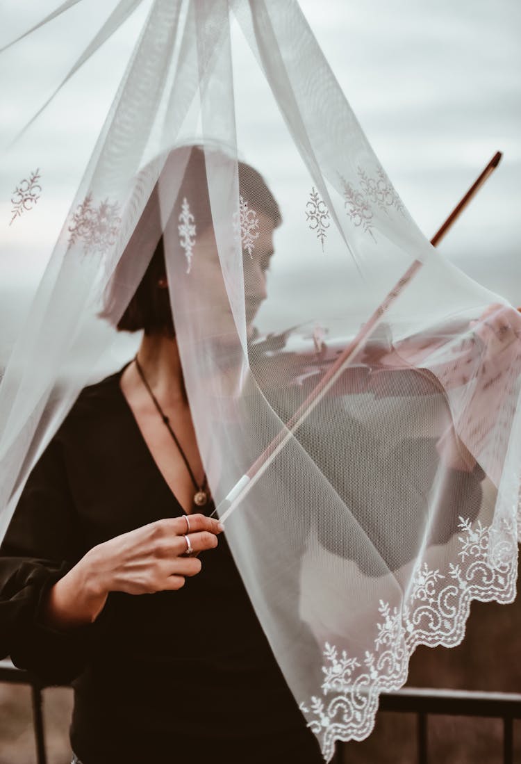 A Woman Playing The Violin Behind Lace Curtain