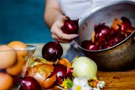Crop anonymous female peeling red and white onions into pan to naturally color Easter eggs for holiday