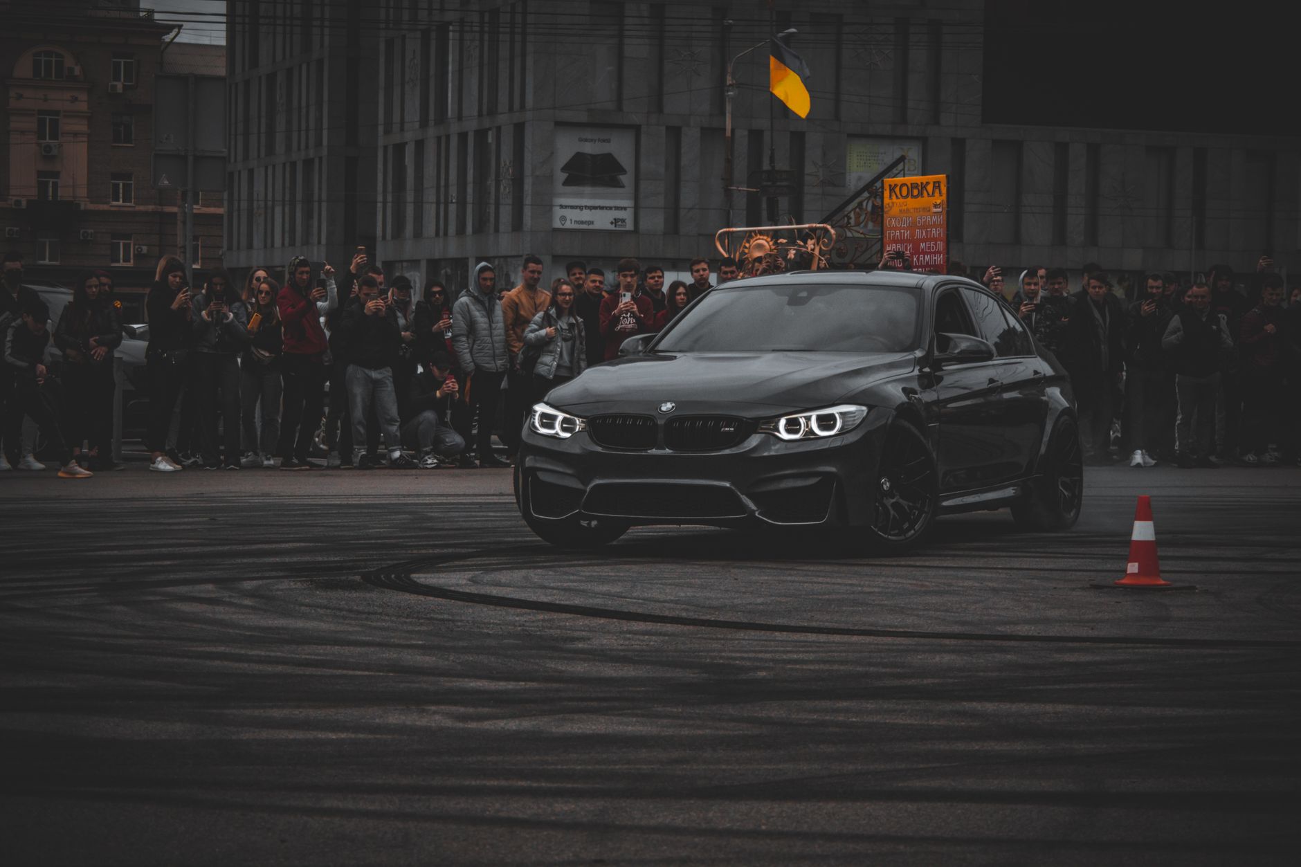 A sleek BMW drifts in front of a crowd during a nighttime city event.