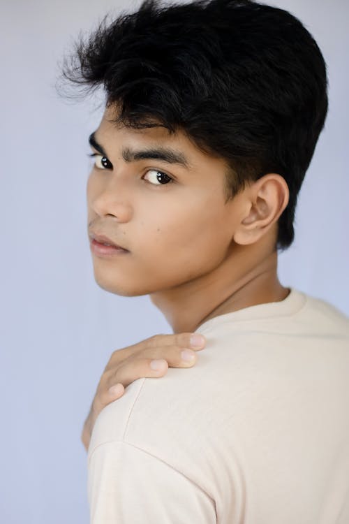 Handsome ethnic teenage male model touching shoulder and looking at camera