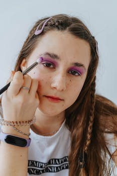 Close-up of a teen girl applying vibrant purple eyeshadow with a brush.