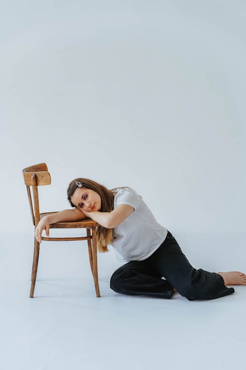 Woman in White Shirt Leaning Her Head on the Brown Wooden Chair