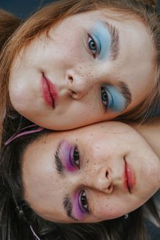 Close-up of two women with vibrant eye makeup and freckles, showcasing beauty and diversity.