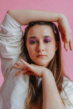 Creative portrait of a woman with vivid purple eye makeup posing against a pink background.