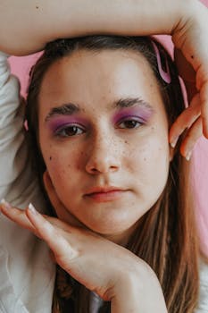 Close-up portrait of a woman with purple eyeshadow and freckles in a studio setting with soft lighting.